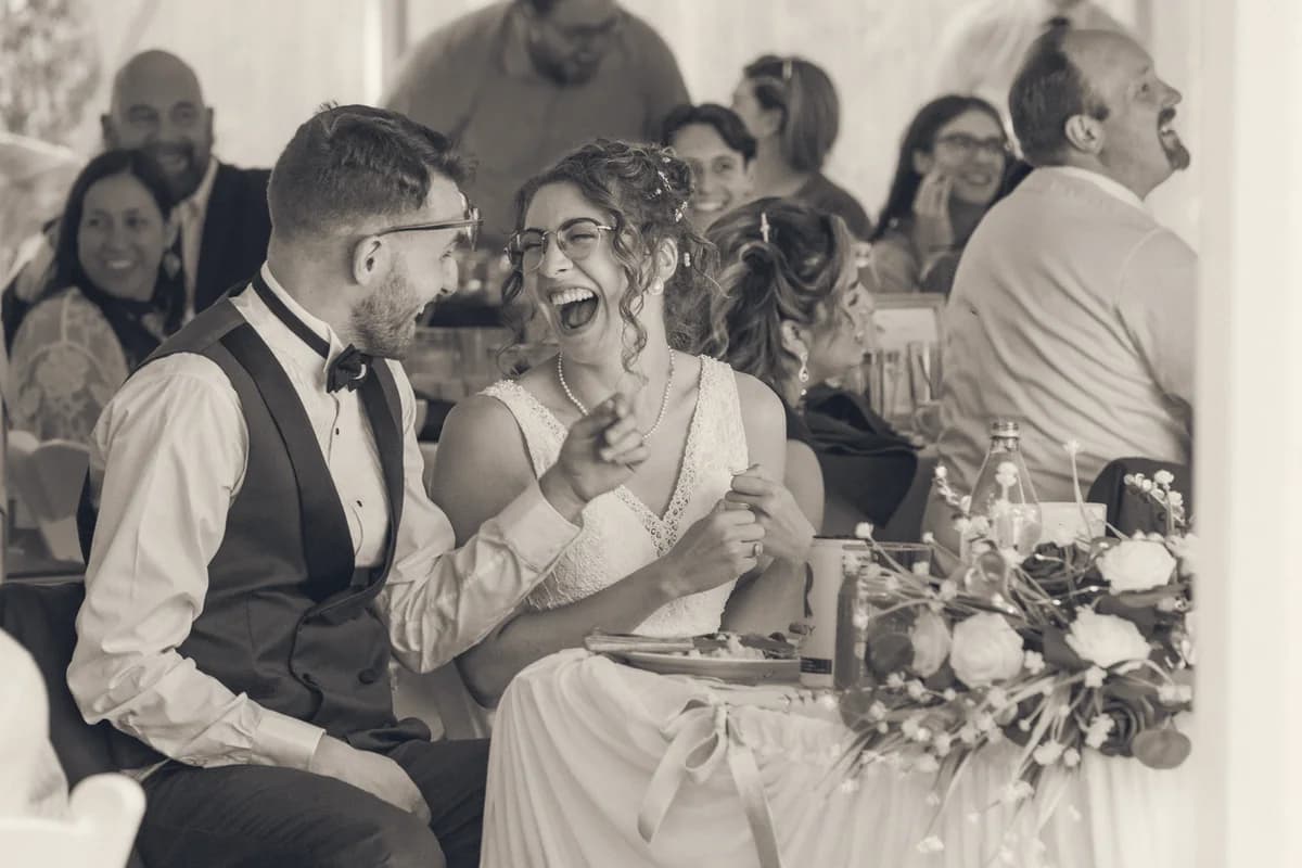 A bride laughing during a wedding speech while the table laughs with her