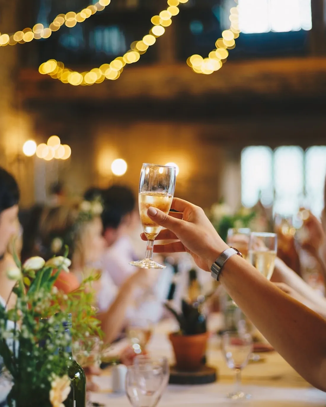 Wedding guests raising champagne glasses under string lights at a reception