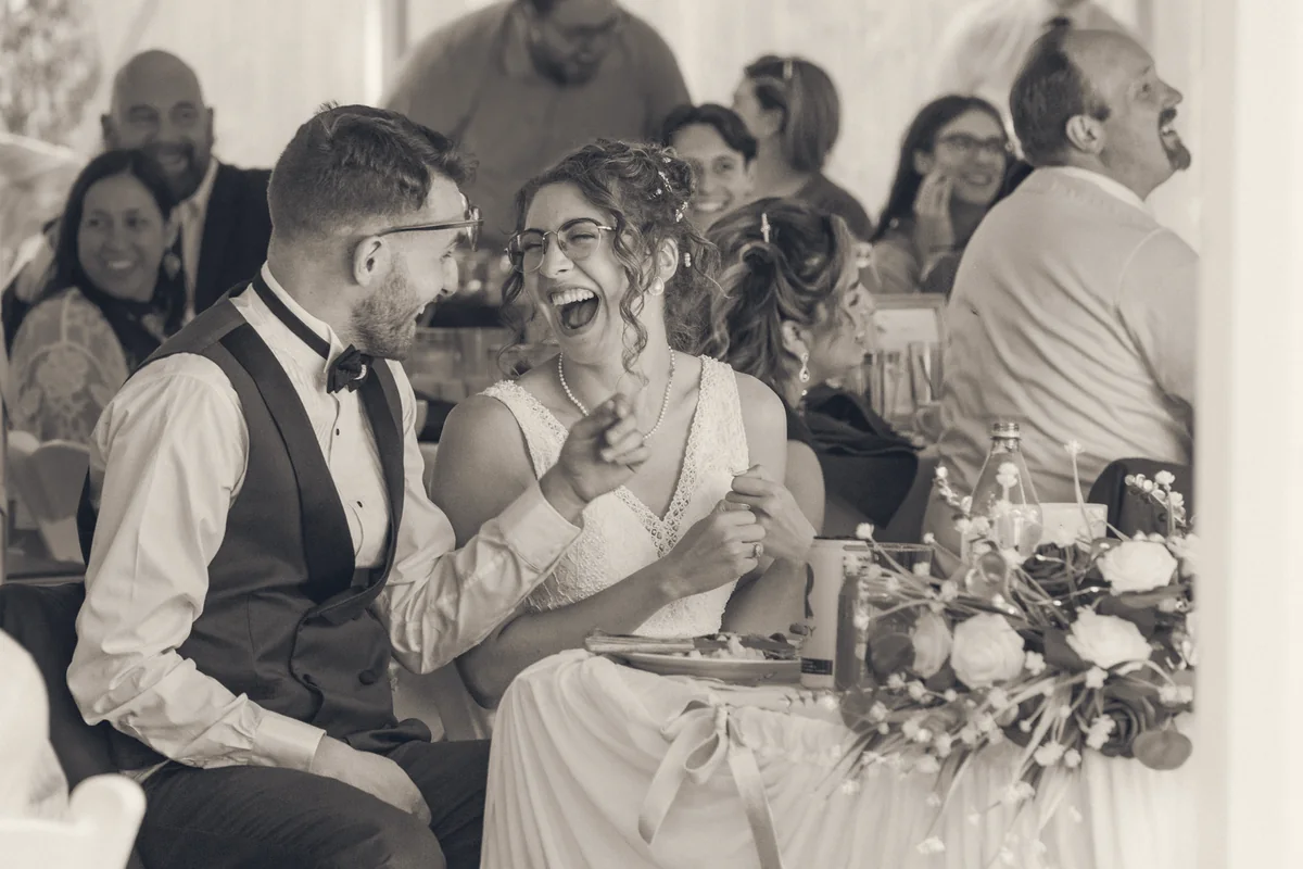 A bride laughing during a wedding speech while the table laughs with her