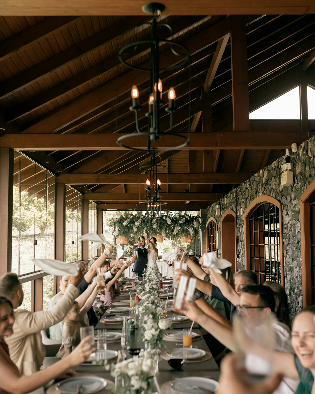 A long reception table of guests raising their glasses toward the couple